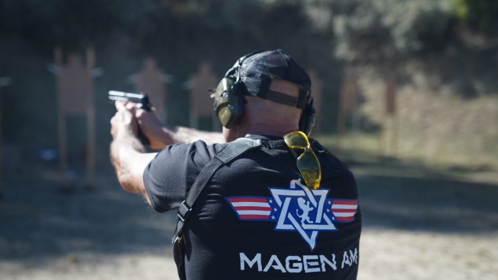 A person wearing a Magen Am shirt holding a firearm,